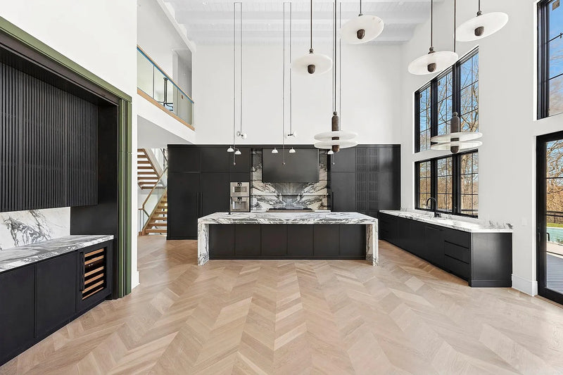 Modern luxury kitchen featuring custom black oak cabinetry, a waterfall marble island, soaring ceilings, architectural millwork, and floor-to-ceiling windows by Cambridge Kitchens.