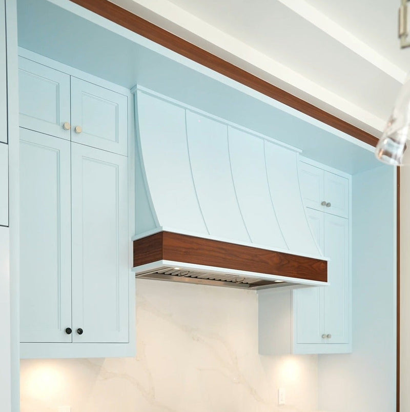 Light blue custom kitchen cabinetry with a walnut-accented range hood, designed and manufactured by Cambridge Kitchens on Long Island.
