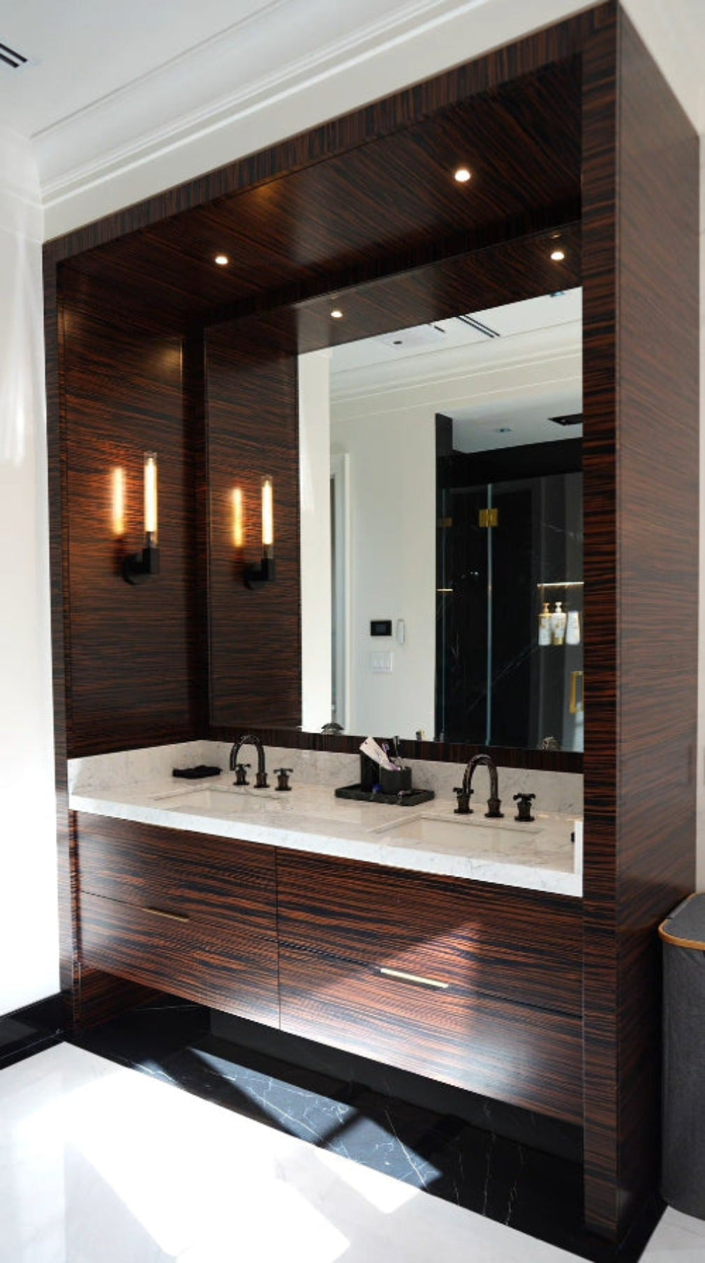 Luxury custom ebony wood double bathroom vanity with integrated wall paneling, oversized mirror and floating cabinetry by Cambridge Kitchens on Long Island.