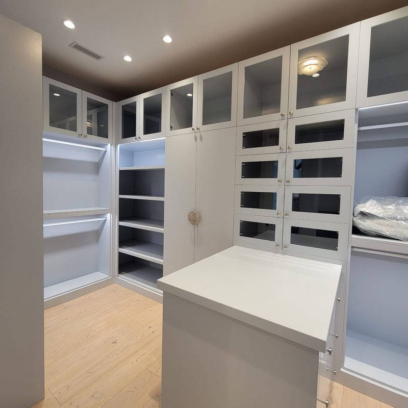 Luxury custom walk-in closet featuring floor-to-ceiling cabinetry, glass display cabinets, custom drawers, and a center island by Cambridge Kitchens.