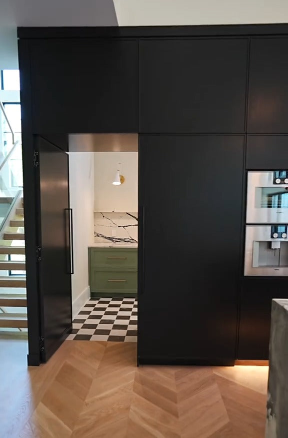 Hidden pantry door integrated into black custom kitchen cabinetry, opening to a secondary pantry by Cambridge Kitchens.